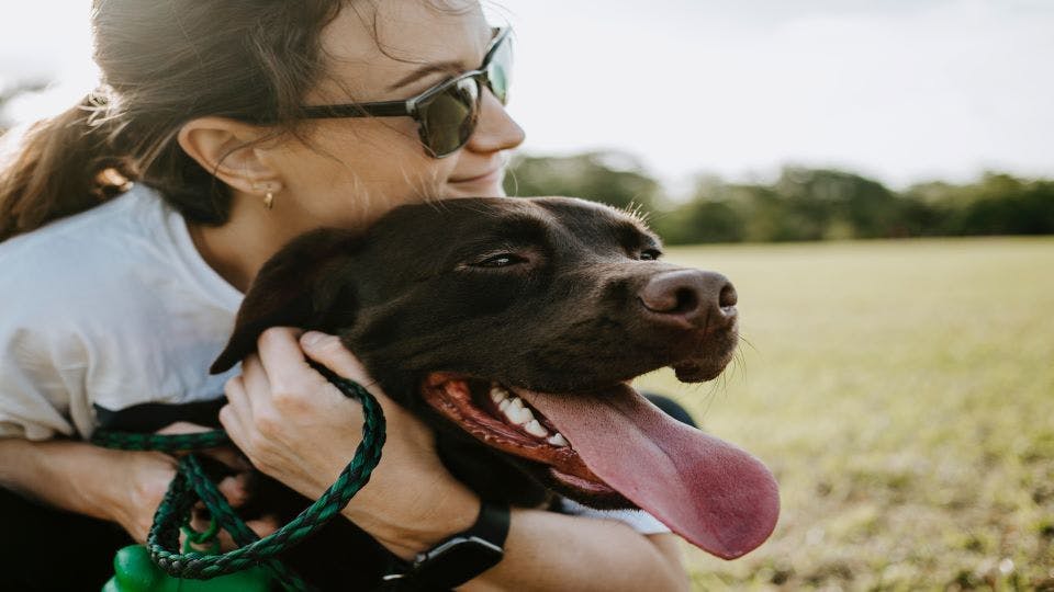 Woman hugging black dog with open mouth 